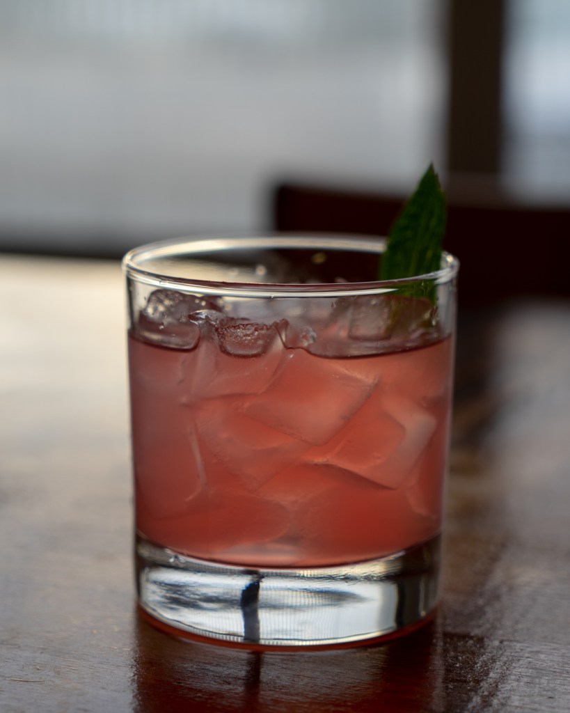 A photo of a pink cocktail with a thai basil leaf garnish