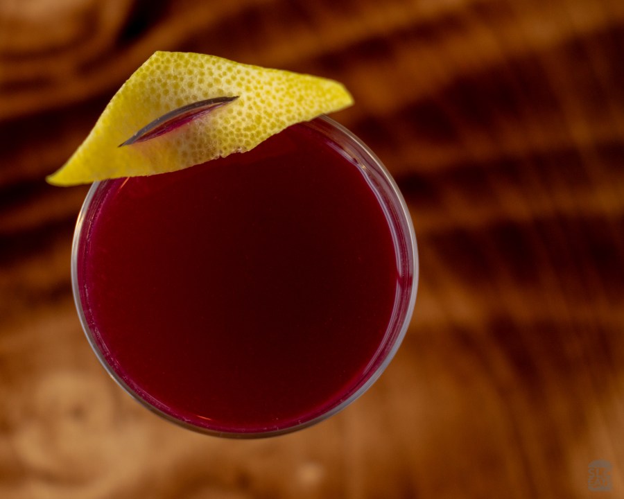 A photo of a red cocktail with a lemon peel garnish
