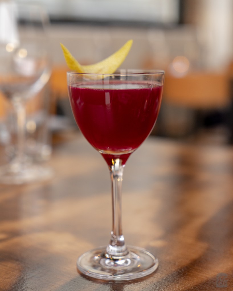 A photo of a red cocktail with a lemon peel garnish