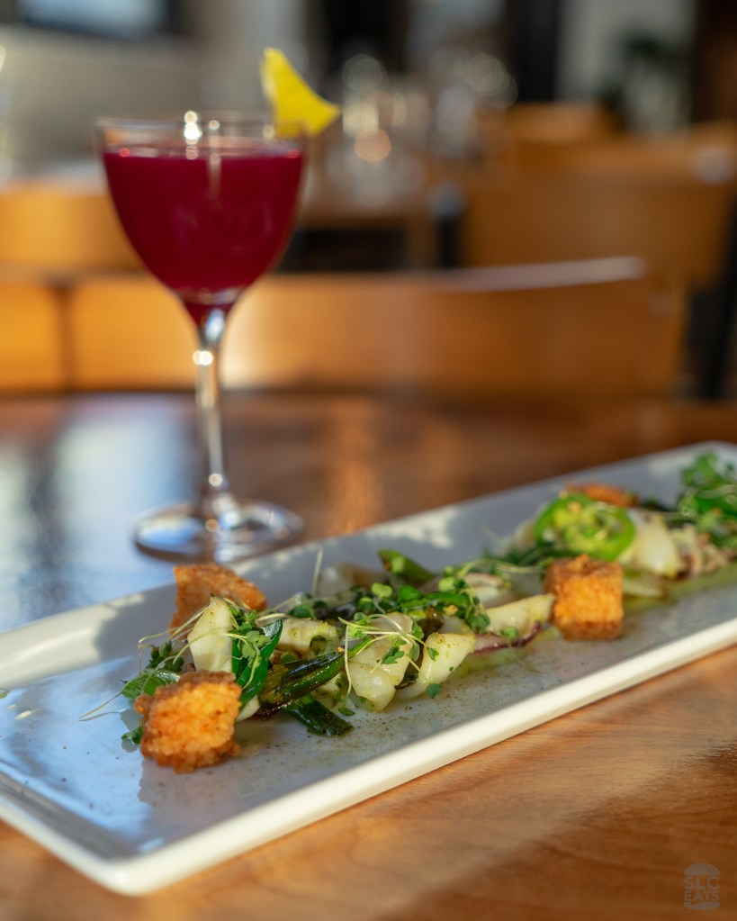 A photo of grilled calamari with a drink in the background