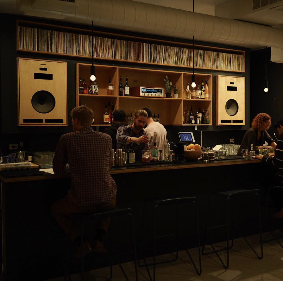 Bartender mixing a cocktail at a bar with vinyl records on the shelf
