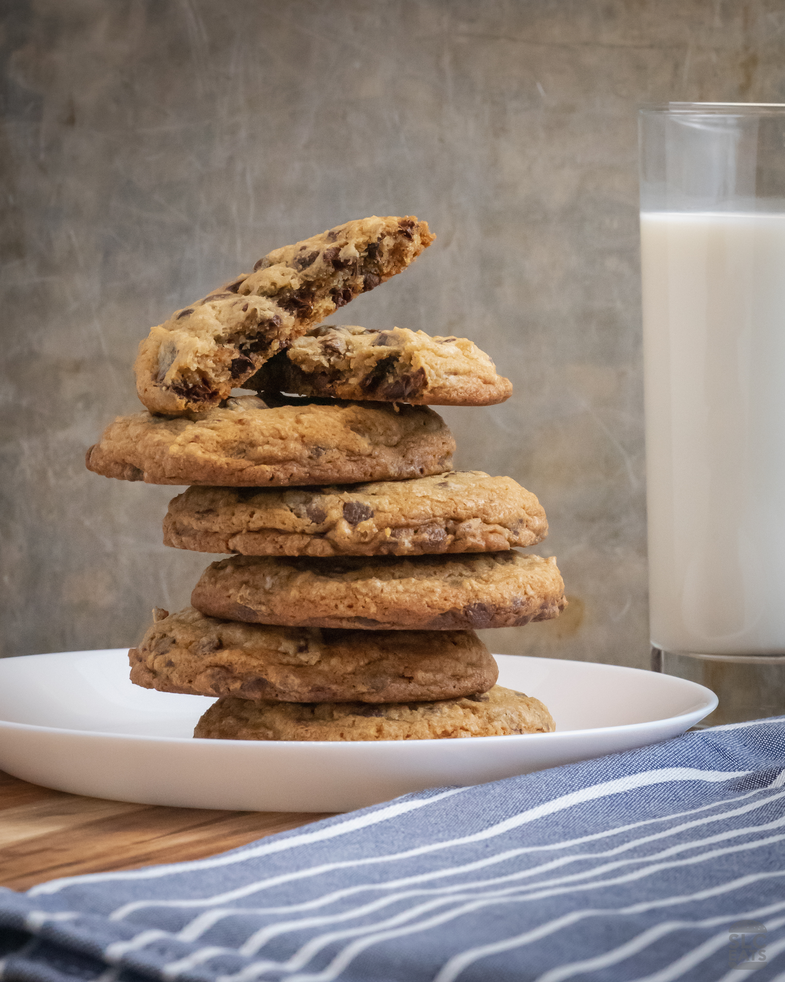 A photo of chocolate chip cookies stacked on top of each other next to a glass of milk